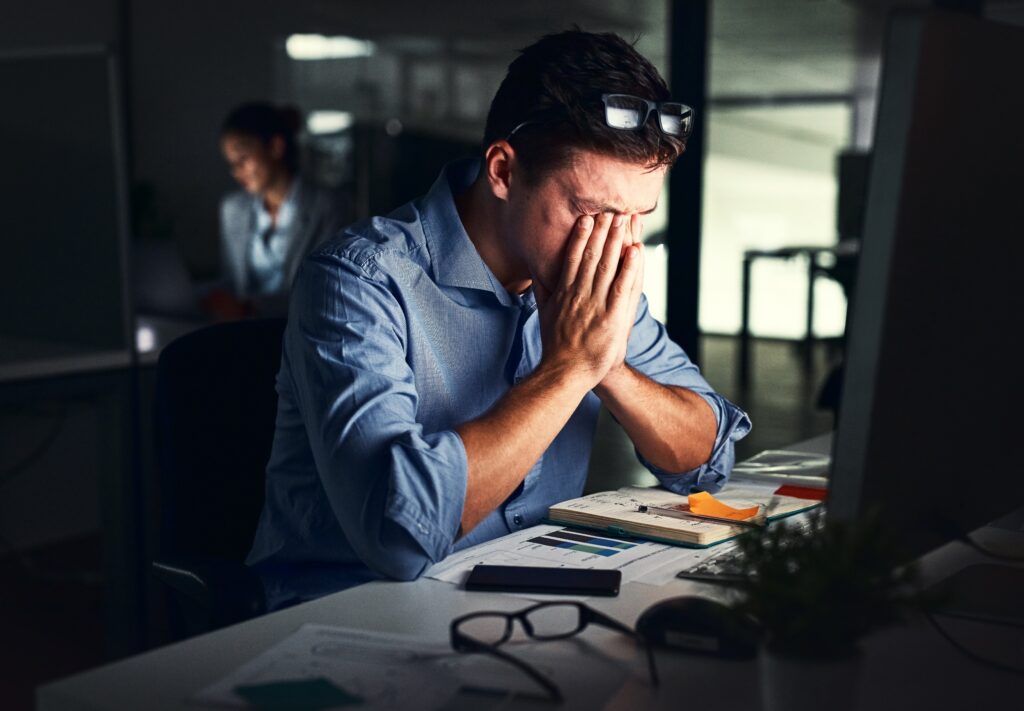 Man zit in een donkere ruimte aan een tafel. Hij is aan het werk en heeft stress